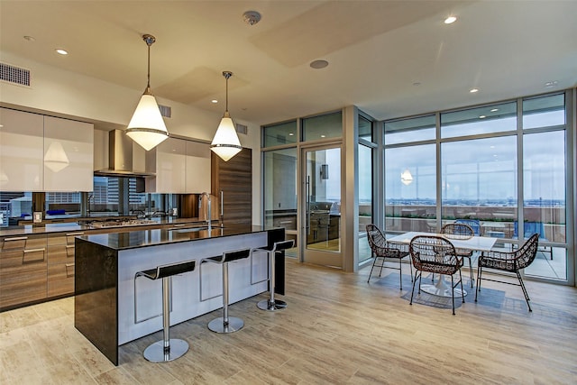 kitchen featuring a center island, sink, wall chimney exhaust hood, a wall of windows, and decorative light fixtures