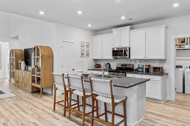 kitchen with white cabinetry, stainless steel appliances, decorative backsplash, washer and clothes dryer, and a center island with sink