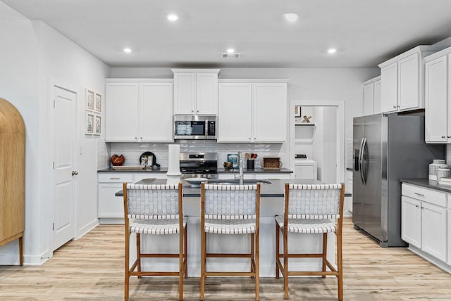 kitchen with a kitchen bar, white cabinetry, a kitchen island with sink, and appliances with stainless steel finishes