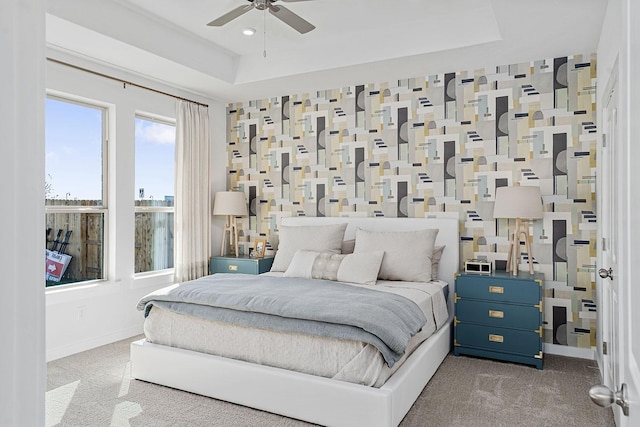 carpeted bedroom featuring a tray ceiling, multiple windows, and ceiling fan