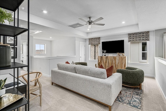 living room featuring a textured ceiling, light colored carpet, a raised ceiling, and ceiling fan