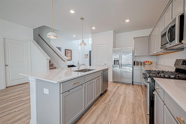 kitchen featuring appliances with stainless steel finishes, a kitchen island with sink, sink, decorative light fixtures, and gray cabinets