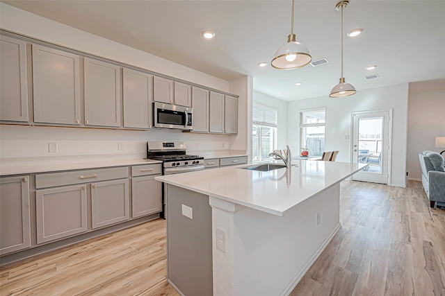 kitchen featuring sink, stainless steel appliances, pendant lighting, gray cabinets, and a kitchen island with sink