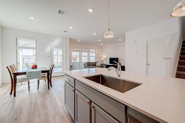 kitchen featuring dishwasher, sink, light hardwood / wood-style flooring, decorative light fixtures, and gray cabinets