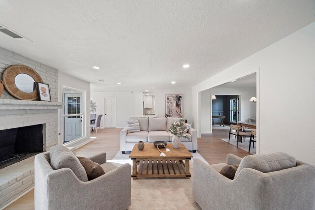 living room with light wood-type flooring, a textured ceiling, and a brick fireplace