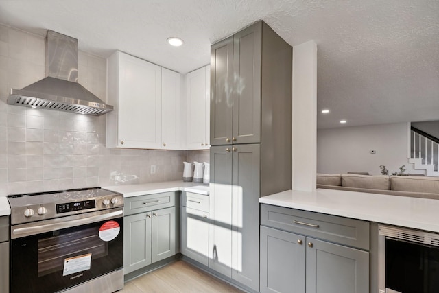 kitchen with electric range, beverage cooler, wall chimney range hood, tasteful backsplash, and gray cabinets