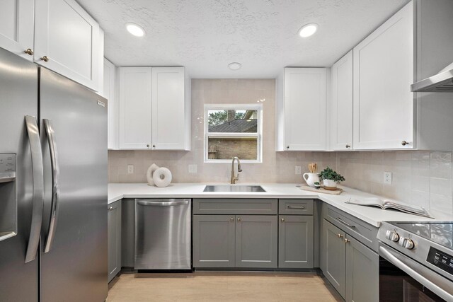 kitchen with gray cabinetry, white cabinetry, sink, stainless steel appliances, and backsplash