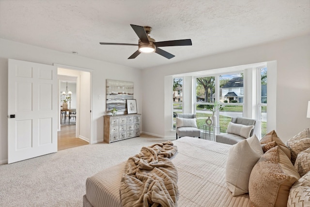 carpeted bedroom featuring a textured ceiling and ceiling fan with notable chandelier