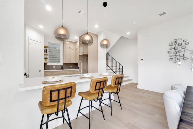 kitchen with sink, hanging light fixtures, light hardwood / wood-style flooring, decorative backsplash, and a breakfast bar