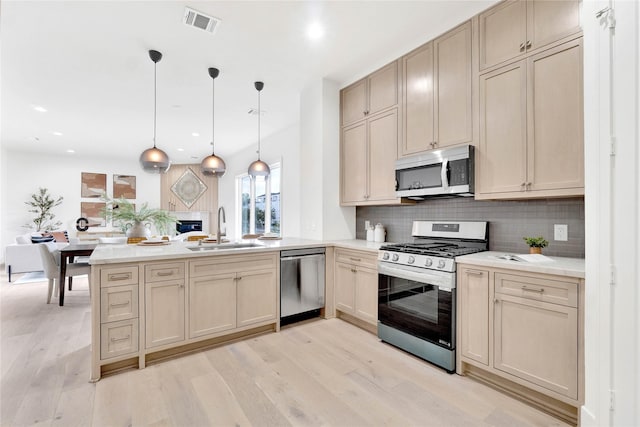 kitchen with backsplash, sink, appliances with stainless steel finishes, decorative light fixtures, and light hardwood / wood-style floors