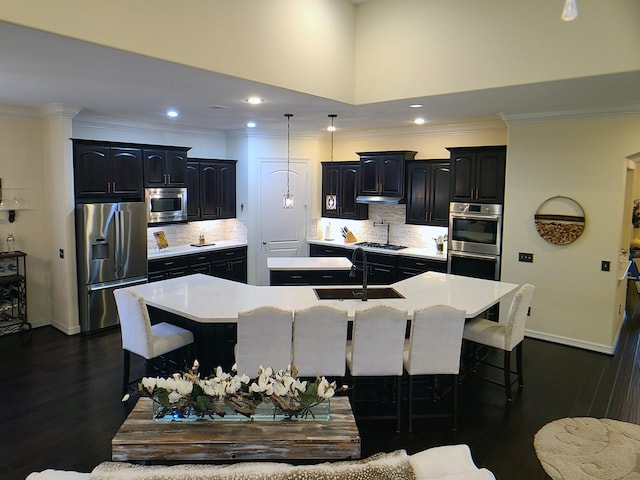 kitchen with a breakfast bar area, decorative backsplash, a kitchen island with sink, and appliances with stainless steel finishes