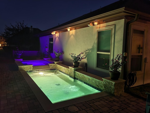 pool at night with an in ground hot tub and pool water feature