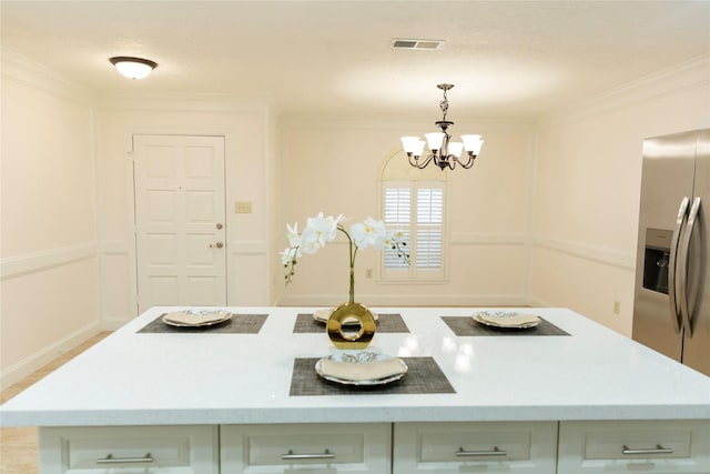 kitchen with white cabinets, ornamental molding, stainless steel fridge, pendant lighting, and a notable chandelier