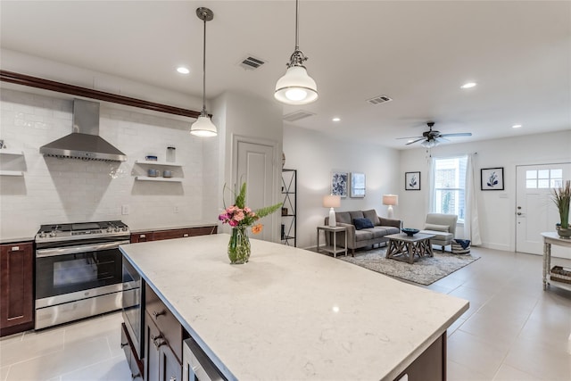 kitchen featuring stainless steel range with electric stovetop, backsplash, wall chimney range hood, ceiling fan, and decorative light fixtures