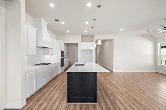 9760 Rockwell Dr, Willis, TX 77318 - kitchen featuring custom range hood, light wood-type flooring, a ceiling fan, decorative backsplash, and an island with sink