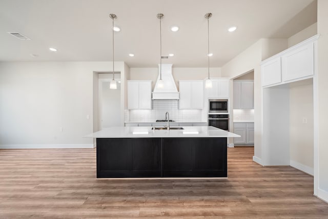 9760 Rockwell Dr, Willis, TX 77318 - kitchen featuring stainless steel appliances, custom range hood, tasteful backsplash, an island with sink, and white cabinetry