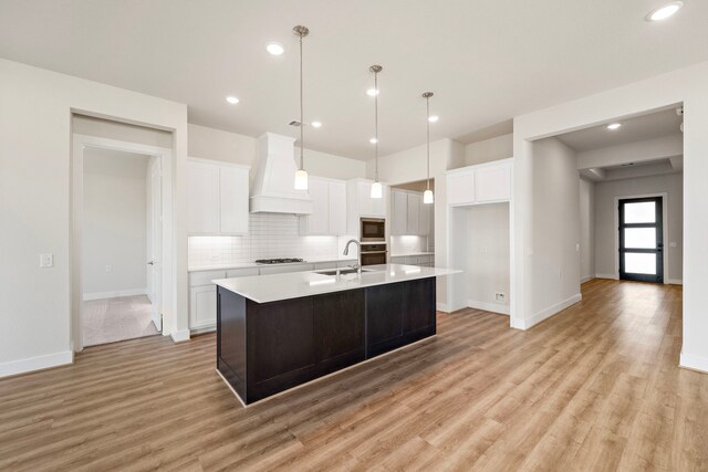 9760 Rockwell Dr, Willis, TX 77318 - kitchen featuring custom range hood, white cabinetry, light countertops, backsplash, and light wood-style floors