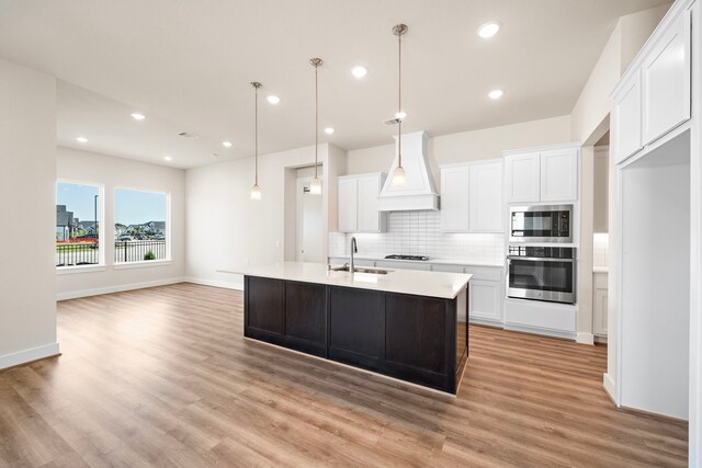 9760 Rockwell Dr, Willis, TX 77318 - kitchen featuring stainless steel appliances, custom range hood, light wood finished floors, backsplash, and white cabinetry