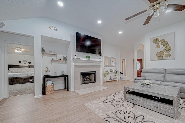 living room featuring light wood-type flooring, vaulted ceiling, and a tiled fireplace