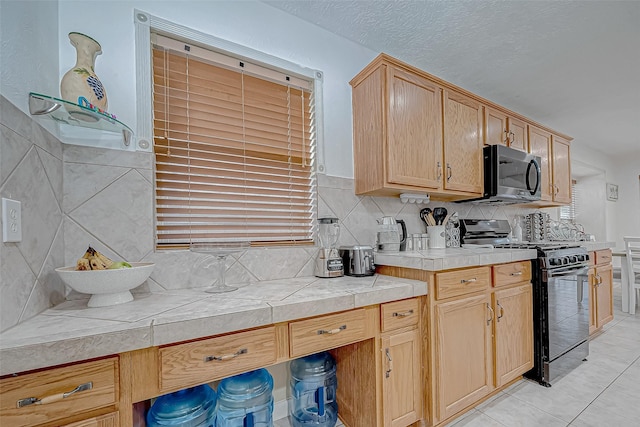 kitchen featuring light brown cabinets, tile countertops, black gas stove, decorative backsplash, and light tile patterned flooring