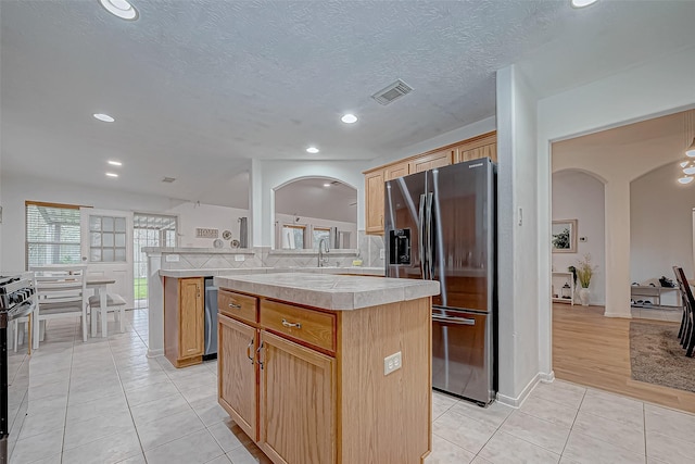 kitchen featuring a center island, light tile patterned floors, a textured ceiling, tile counters, and stainless steel fridge with ice dispenser