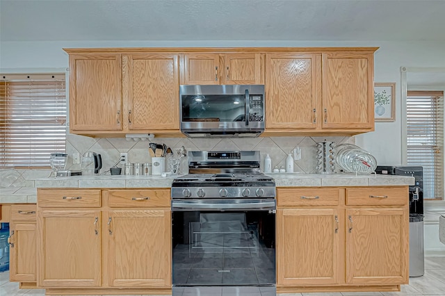 kitchen with light brown cabinets, black range with gas stovetop, light tile patterned floors, and backsplash