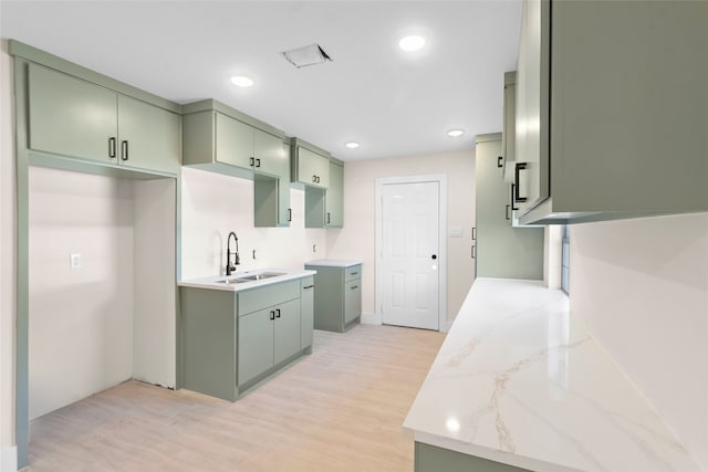 kitchen with green cabinets, light stone counters, sink, and light hardwood / wood-style floors