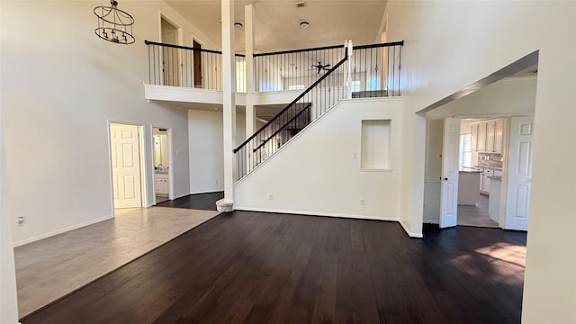 unfurnished living room featuring dark hardwood / wood-style floors, a towering ceiling, and an inviting chandelier