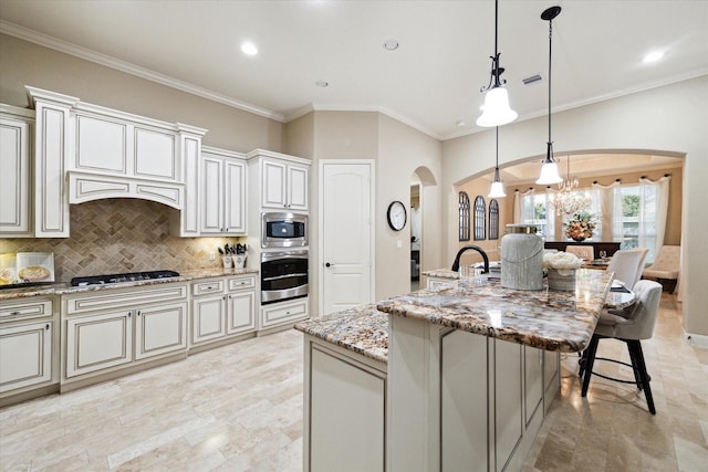 kitchen featuring a kitchen island with sink, hanging light fixtures, light stone countertops, tasteful backsplash, and stainless steel appliances