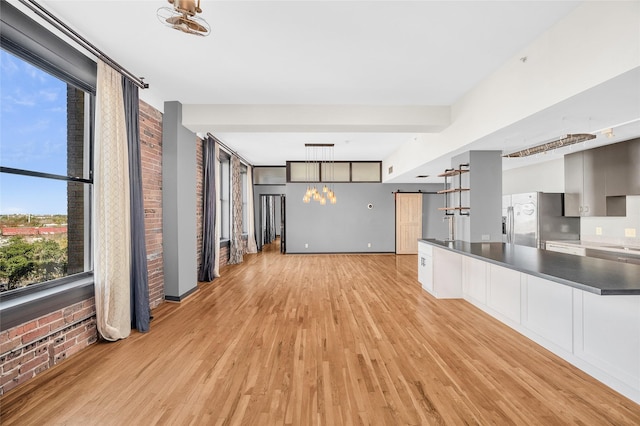 interior space featuring light wood-type flooring, stainless steel fridge with ice dispenser, a barn door, and brick wall