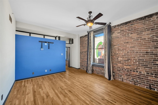 empty room with hardwood / wood-style flooring, ceiling fan, and brick wall