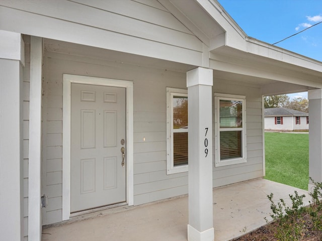 view of exterior entry featuring a porch and a yard