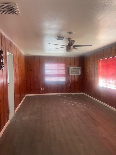 empty room with a wall unit AC, plenty of natural light, and wood walls