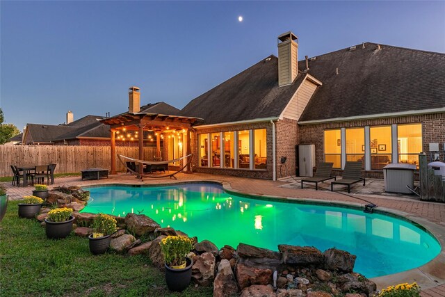 pool at dusk featuring a patio area and a pergola