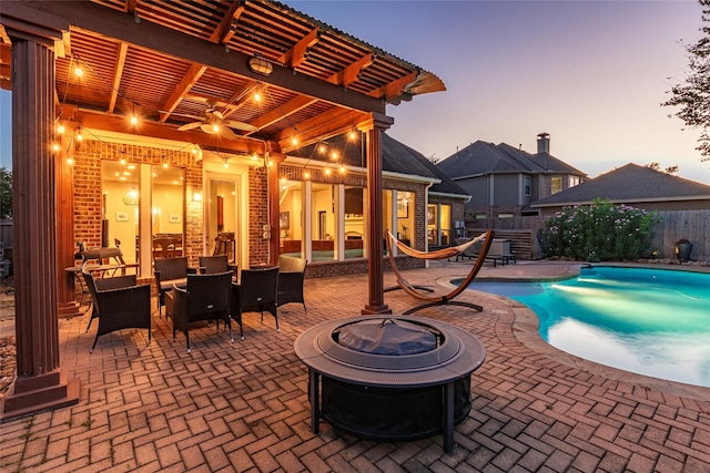 pool at dusk featuring a pergola, a patio, an outdoor fire pit, and ceiling fan