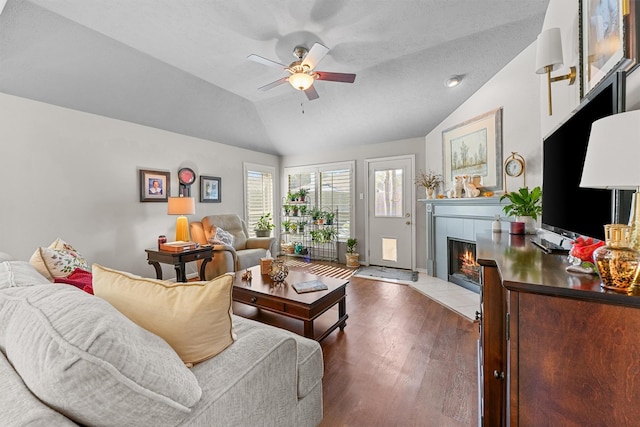 living area featuring a ceiling fan, lofted ceiling, dark wood finished floors, and a tile fireplace