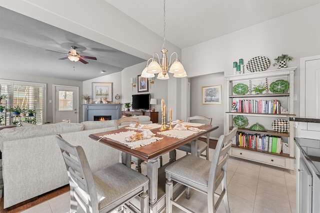 dining room featuring lofted ceiling, ceiling fan with notable chandelier, a tiled fireplace, and light tile patterned flooring