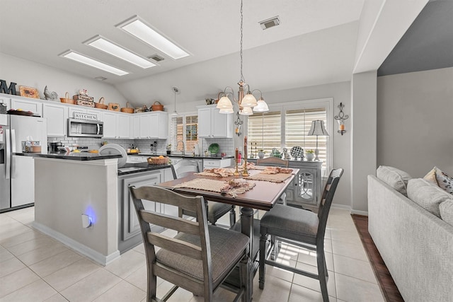 dining room with lofted ceiling, light tile patterned floors, visible vents, and a notable chandelier