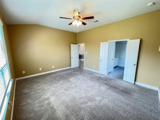 unfurnished bedroom featuring dark colored carpet, ensuite bathroom, vaulted ceiling, and ceiling fan