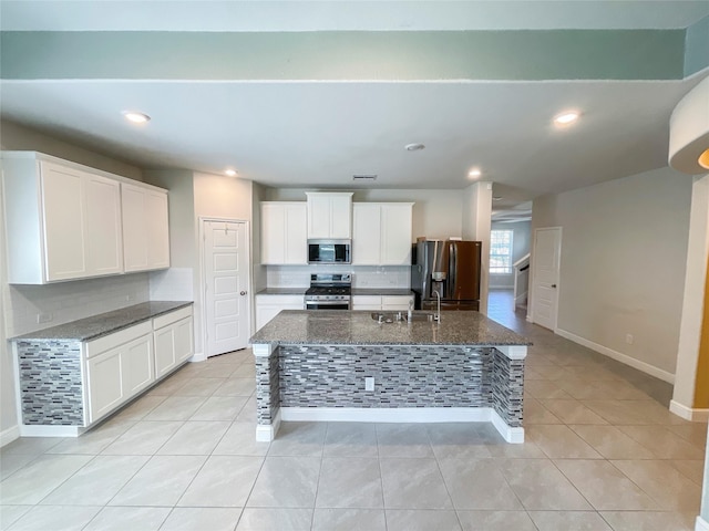 kitchen featuring a center island with sink, dark stone countertops, white cabinetry, and appliances with stainless steel finishes