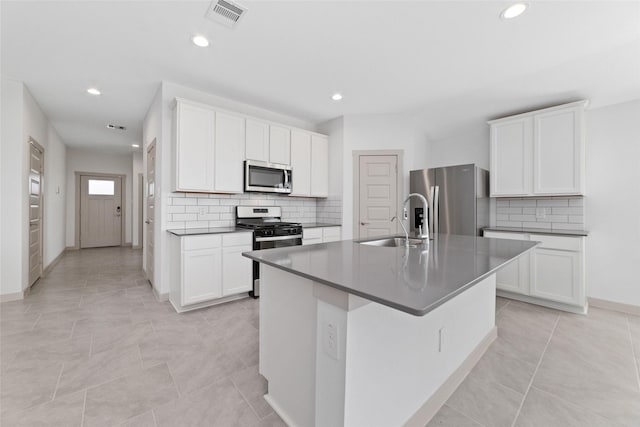 kitchen with appliances with stainless steel finishes, sink, white cabinets, an island with sink, and light tile patterned flooring