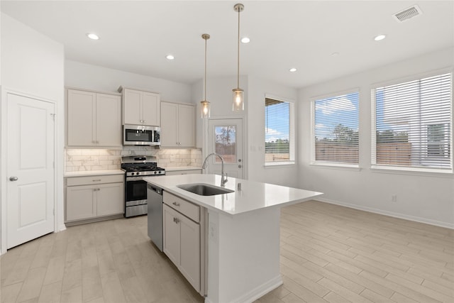 kitchen with pendant lighting, stainless steel appliances, a center island with sink, and sink