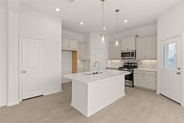 kitchen with sink, stainless steel appliances, backsplash, an island with sink, and decorative light fixtures