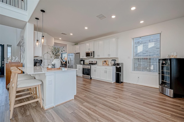 kitchen featuring hanging light fixtures, light wood-type flooring, white cabinetry, stainless steel appliances, and beverage cooler