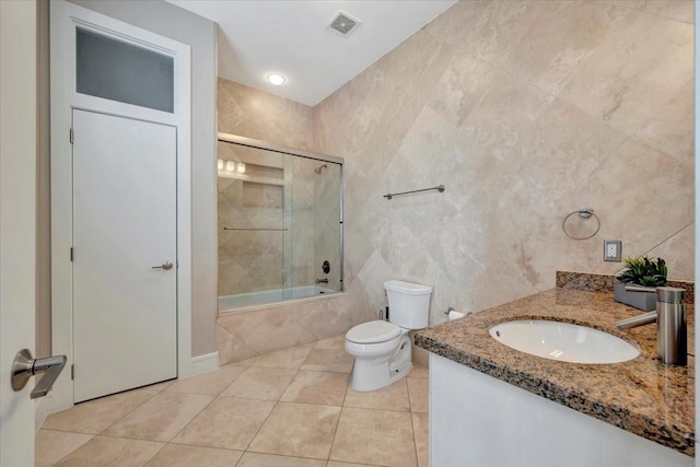 full bathroom featuring tile patterned flooring, combined bath / shower with glass door, toilet, vanity, and tile walls