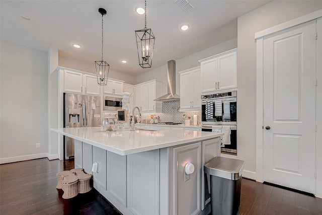 kitchen with pendant lighting, a center island with sink, wall chimney exhaust hood, white cabinetry, and stainless steel appliances