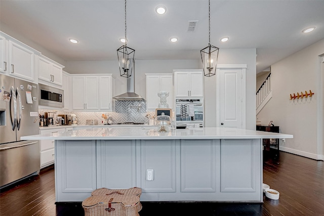 kitchen featuring an island with sink, white cabinets, stainless steel appliances, and wall chimney range hood