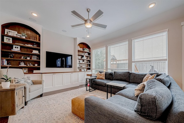 living room featuring built in shelves, ceiling fan, and light hardwood / wood-style flooring