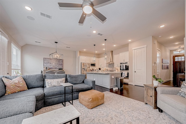 living room featuring light wood-type flooring, ceiling fan with notable chandelier, and sink