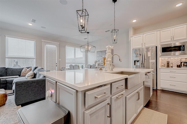 kitchen featuring pendant lighting, stainless steel microwave, a kitchen island with sink, sink, and white cabinetry